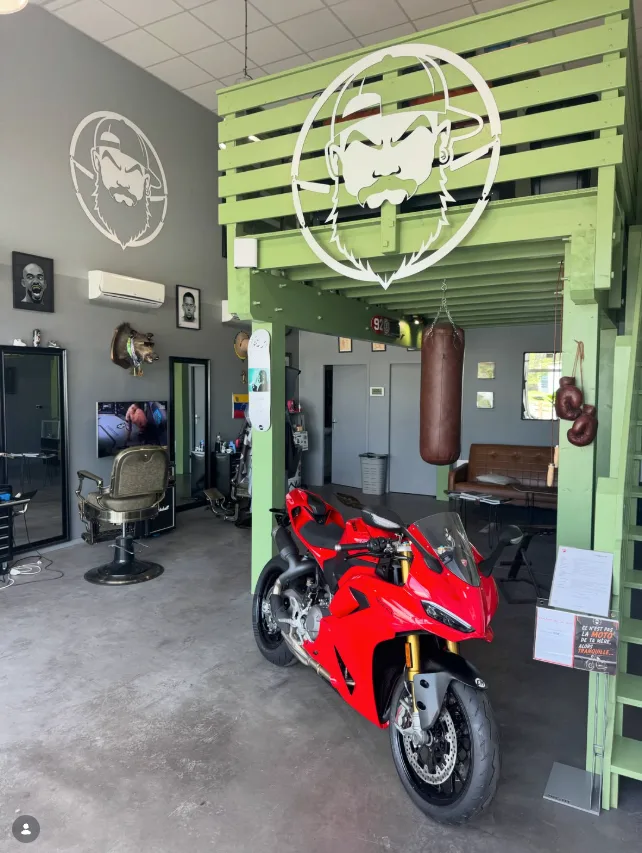 La Ducati Panigale V2 rouge exposée sous la mezzanine verte du salon Porrada Barber Shop, à côté du fauteuil barbier