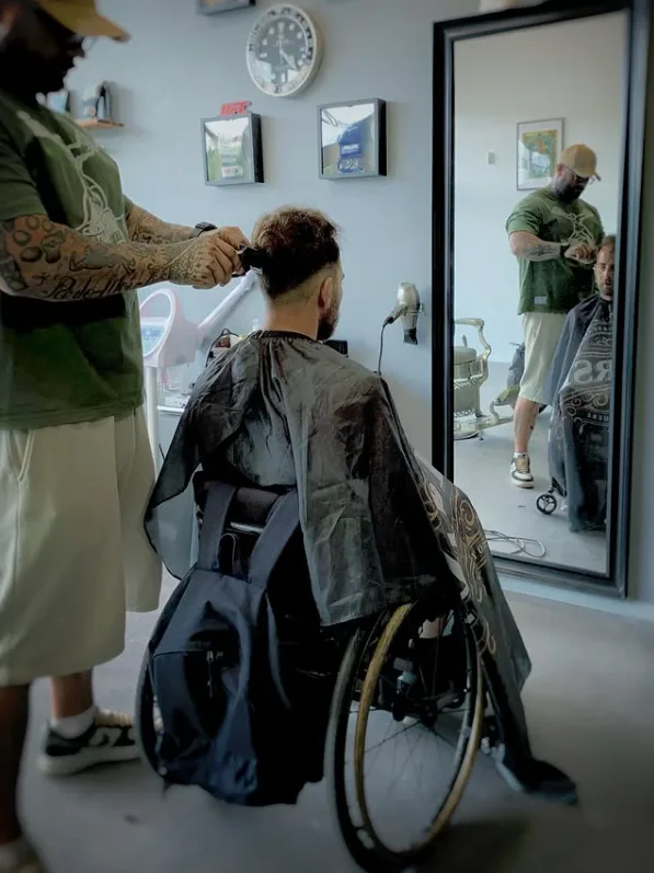 Un barbier Porrada coupe les cheveux d'un client installé sur son fauteuil roulant, dans le salon du Village Iraty à Biarritz